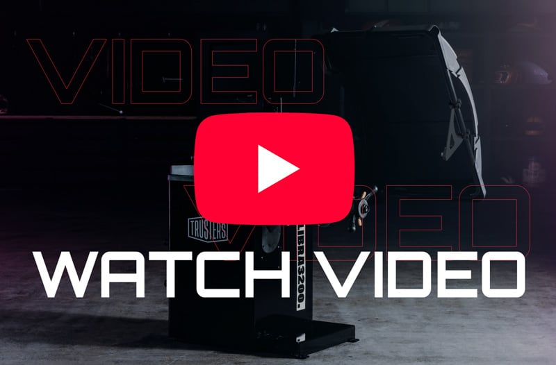 Dark workshop scene with a black industrial machine centered, large white WATCH VIDEO text across the bottom and a red YouTube play button icon overlaid in the middle.