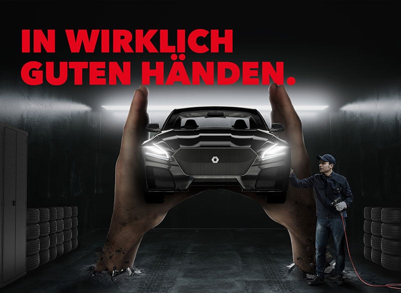 Großes Plakat mit roter Überschrift IN WIRKLICH GUTEN HÄNDEN, zwei riesige Hände halten frontal ein beleuchtetes Auto in einer dunklen Werkstatt, rechts steht ein Mechaniker mit Druckluftschlauch, Stapel Reifen links