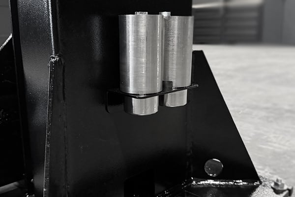 Schwarz-weißaufnahme einer geschweißten schwarzen Metallbasis mit einer Halterung, in der zwei nebeneinander stehende silberne Zylinderstifte durch eine Klammer gesichert sind