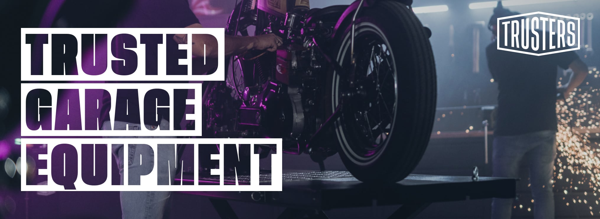 Motorrad auf Hebebühne mit sichtbaren Mechanikerhänden, lila Beleuchtung und Funken, großer weißer Schriftzug TRUSTED GARAGE EQUIPMENT links, TRUSTERS-Logo rechts oben