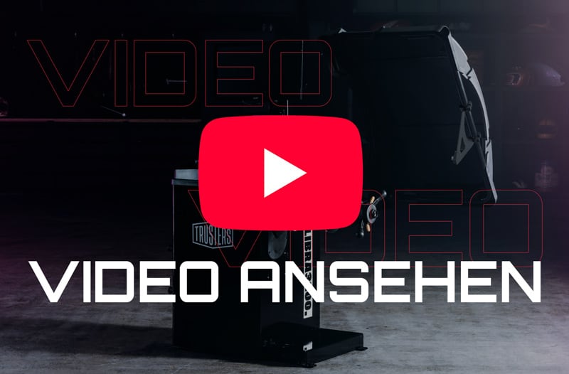 Großes rotes YouTube-Play-Symbol über dunkel gehaltenem Industriehintergrund mit einer schwarzen Maschine, darunter weißer Schriftzug VIDEO ANSEHEN