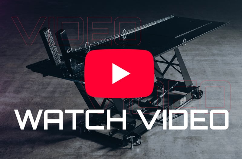 Black hydraulic scissor-lift table on a concrete floor with a large red play-button icon over the platform and bold white text WATCH VIDEO across the lower area