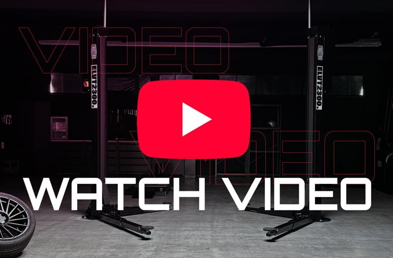 Dim automotive garage with a two-post car lift, spare wheel, large red YouTube play button overlay and bold white WATCH VIDEO text