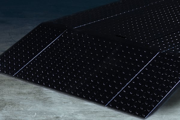 Pair of black rubber vehicle ramps with raised circular non-slip pattern and angled slopes placed side by side on a concrete floor