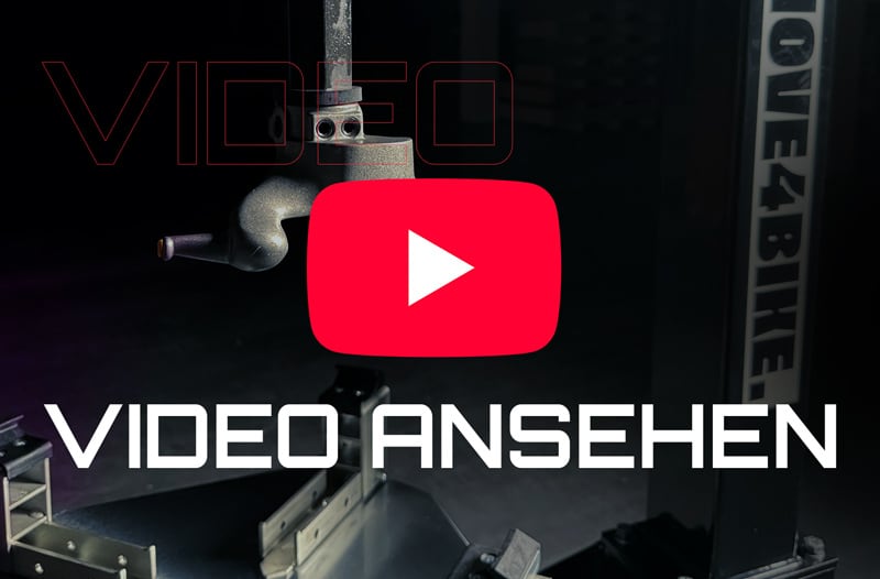 Rotes YouTube-Play-Symbol zentral über dunkler Werkstatt-/Studioaufnahme mit Metallarm und Halterungen, Schriftzug VIDEO ANSEHEN in weiß unten