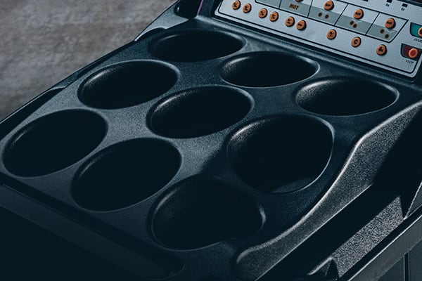 Unidad de plástico negro con ocho cavidades circulares (posavasos) y una franja superior con botones y luces indicadoras