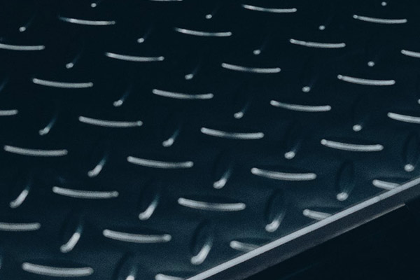 Nahaufnahme einer dunklen Metall-Trittplatte mit diagonaler Kante und regelmäßigem Muster aus erhabenen ovalen Noppen