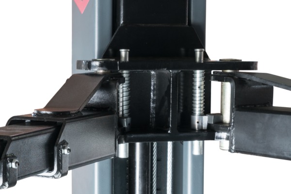 Close-up of a black metal two-post car lift arm assembly with vertical column, adjustable support arms, visible coil springs, mounting plate, bolts and hydraulic cables