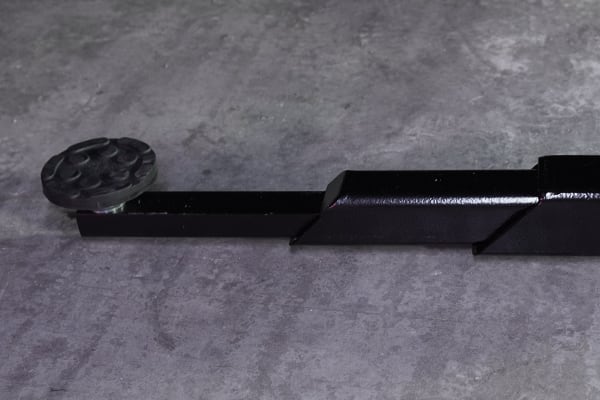 Schwarze Teleskop-Metallstange mit rundem, dekorativem Endknauf links, auf grauem, strukturiertem Beton- oder Steinuntergrund liegend