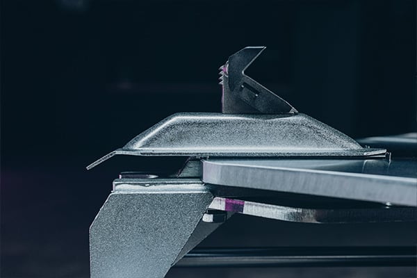 Seitliche Nahaufnahme einer metallischen Klemme mit gezahntem Hebel und flacher Auflage, Teil einer Schneid- oder Pressevorrichtung, kühle Beleuchtung und dunkler Hintergrund