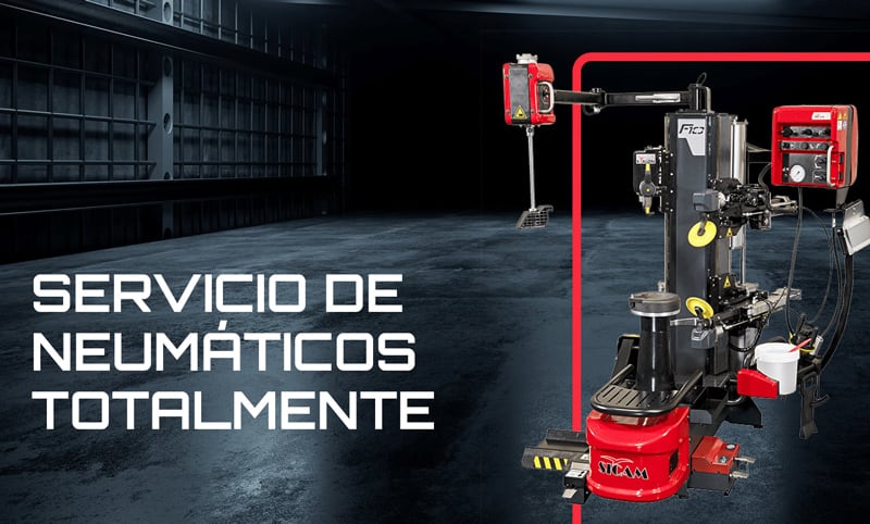 Taller oscuro con suelo de hormigón, máquina desmontadora de neumáticos roja a la derecha y texto blanco grande a la izquierda: SERVICIO DE NEUMÁTICOS TOTALMENTE