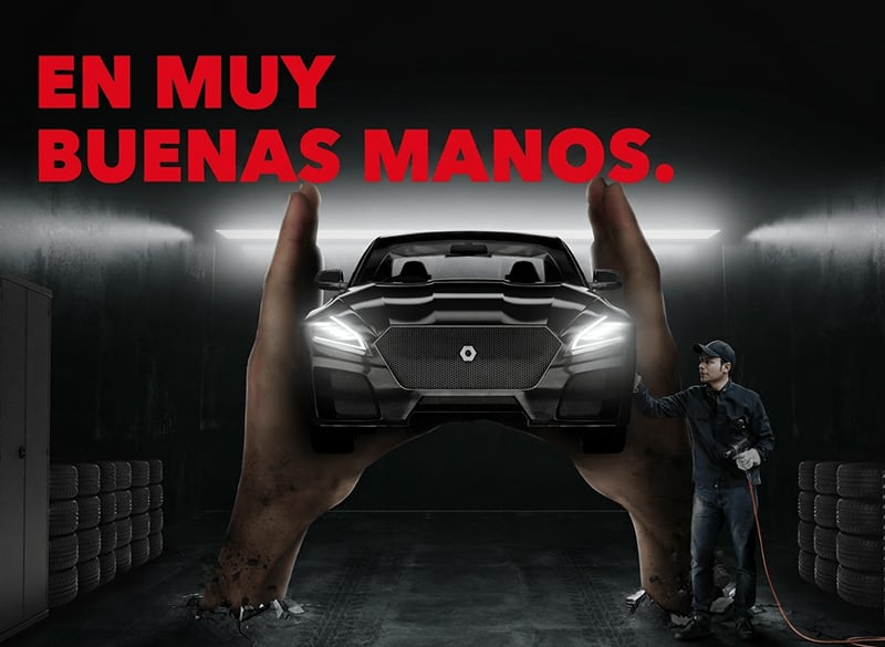 Manos gigantes sostienen un coche negro en un taller oscuro; a la derecha un mecánico con herramienta, pilas de neumáticos a ambos lados y el texto rojo grande EN MUY BUENAS MANOS arriba.