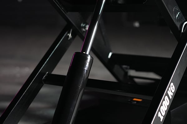 Close-up of a black hydraulic piston and scissor-lift metal frame with 1000 KG weight label visible