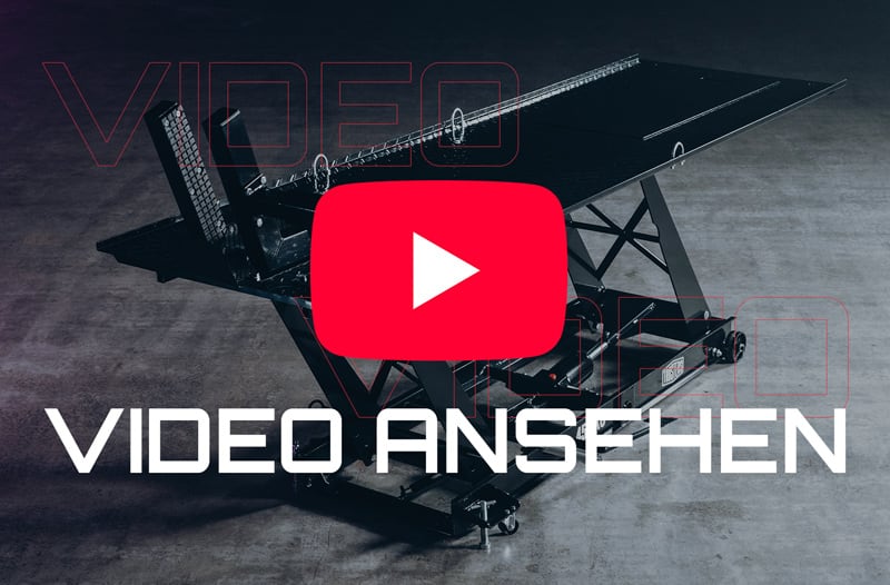 Schwarzer Scherenhubtisch auf Betonboden, darüber mittig großes rotes Play-Symbol und weißer Schriftzug VIDEO ANSEHEN, dezente rote Kontur-Schrift "VIDEO" im Hintergrund