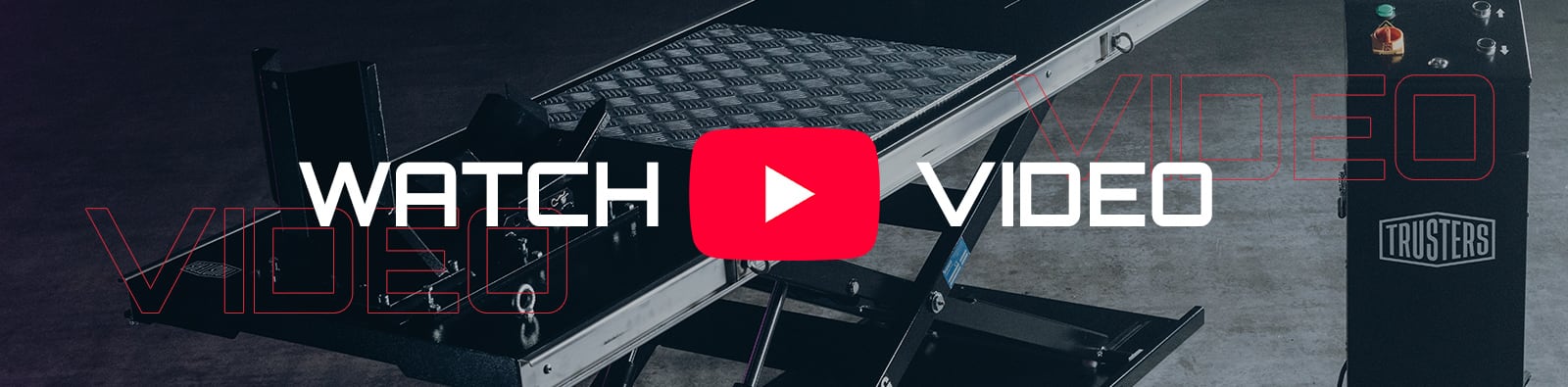 Hydraulic scissor lift table in a workshop with a large red YouTube play icon centered and overlaid text WATCH VIDEO, faint red outlined VIDEO lettering across the background, and a control box labeled TRUSTERS on the right