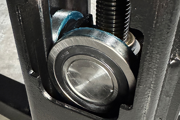 Close-up of a shiny circular metal bearing and adjacent threaded rod seated in a dark gray cast-iron housing, showing bearing race and machined surfaces