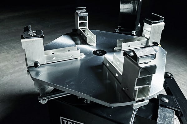Placa metálica triangular con cuatro mordazas ajustables de aluminio montadas sobre una base negra, herramienta industrial para sujetar piezas