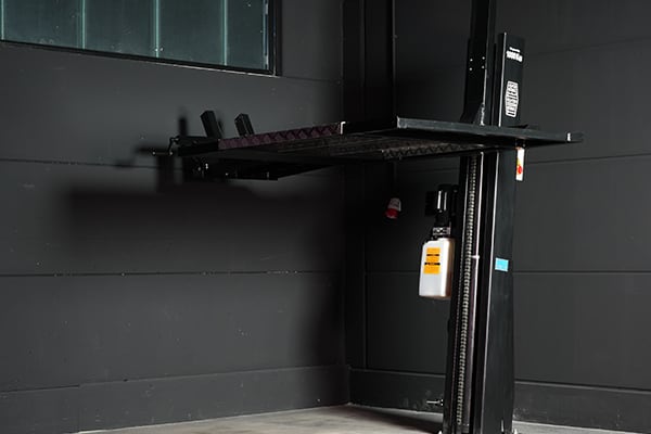 Elevador de coche de un solo poste en un garaje oscuro, plataforma elevada, columna vertical negra con una botella de aceite colgada y suelo de hormigón