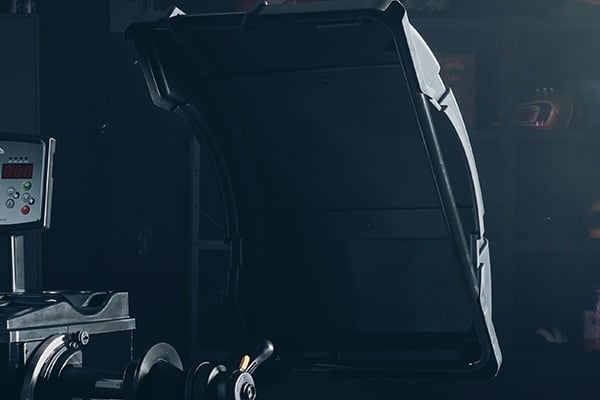 Geöffnete Motorhaube eines Fahrzeugs in dunkler Werkstatt, im Vordergrund Werkzeug und eine Maschine mit kleinem digitalen Bedienfeld