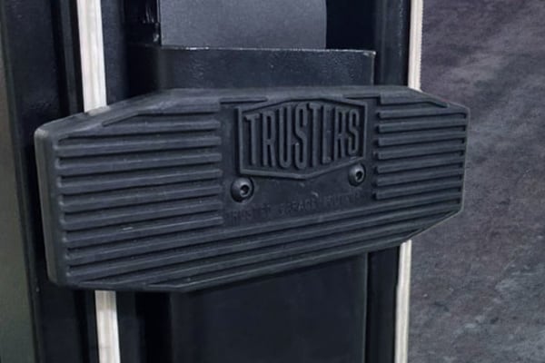 Close-up of a black ribbed rubber pad with an embossed TRUSTLIFTS logo mounted between two vertical metal rails