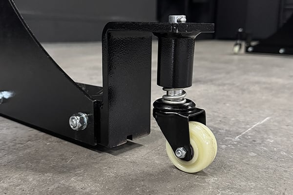 Rueda giratoria de nylon color crema montada en un soporte metálico negro con pernos y arandelas, primer plano sobre suelo de hormigón
