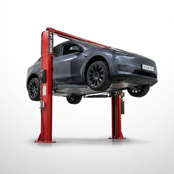 Graues Tesla-Auto auf rotem Zwei-Säulen-Autolift angehoben, Vorder- und Unterseite sichtbar, isoliert vor weißem Hintergrund