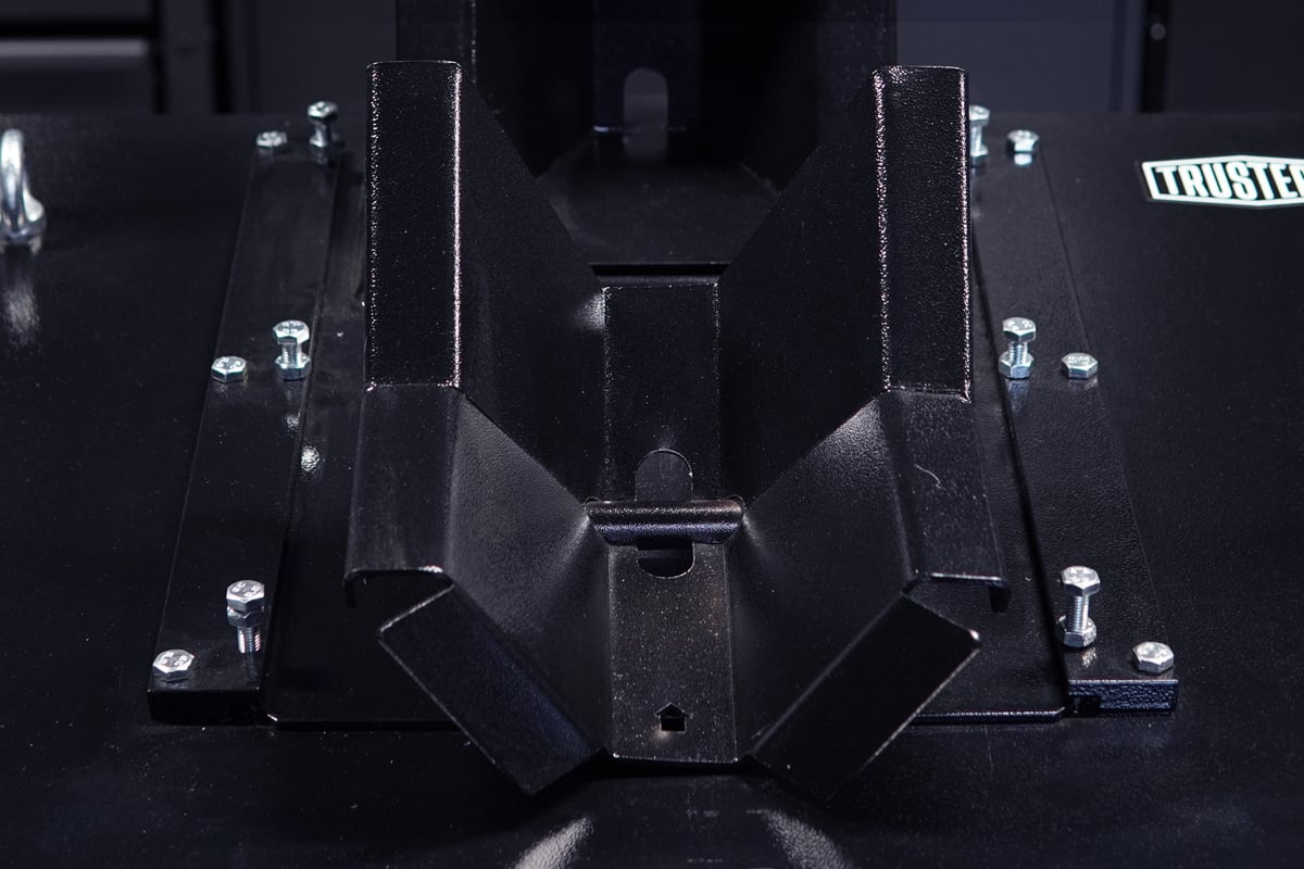Soporte metálico negro en forma de canal montado sobre una placa negra con tornillos hexagonales visibles, vista en primer plano