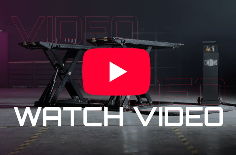 Scissor-lift platform in a dim industrial garage with a centered red YouTube play icon overlay, large white WATCH VIDEO text at the bottom, and a control pedestal to the right