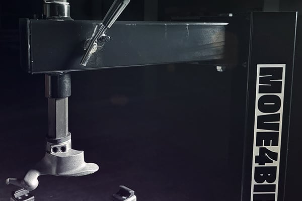 Detalle de soporte metálico de estudio: columna vertical con rótulo MOVE4BIL, brazo horizontal y pieza de montaje en primer plano sobre fondo oscuro