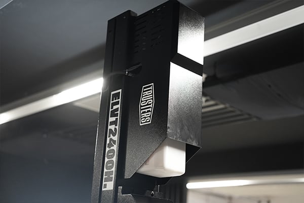 Nahaufnahme eines schwarzen, an einer Deckenschiene montierten Bühnenlichts mit sichtbarer Aufschrift ELIT2400H, weißem Diffusor und metallischem Gehäuse, unscharfe Deckenbeleuchtung im Hintergrund