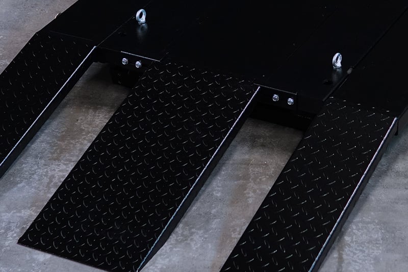 Three black steel diamond-plate ramps attached to a flat platform with two lifting eye bolts, positioned on a concrete floor