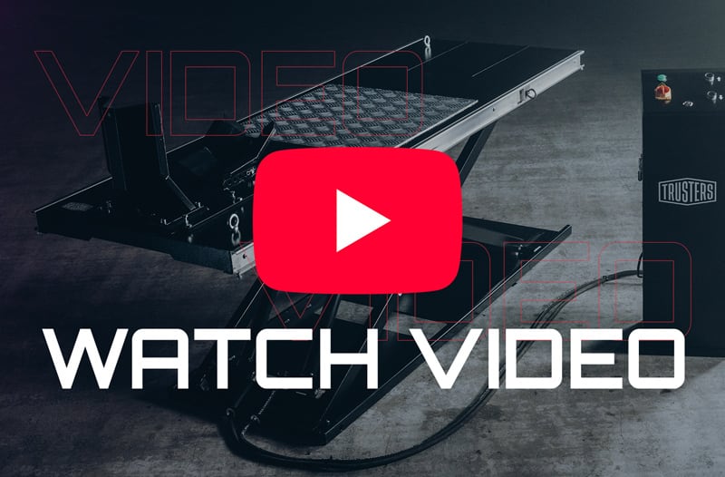 Industrial scissor-style vehicle lift on a concrete floor with hydraulic control box to the right, overlaid by a large red YouTube play button icon and bold white text reading WATCH VIDEO.