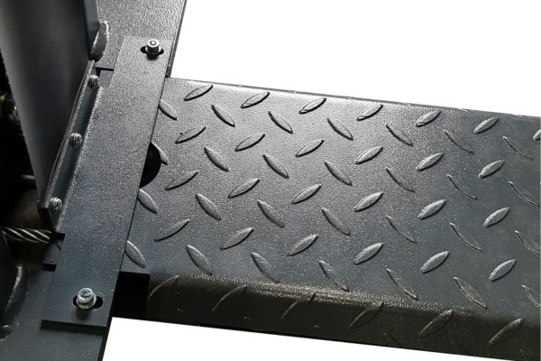 Close-up of dark gray diamond-plate metal platform with raised textured pattern, attached to a metal support bracket with visible bolts and a cable passing through a cutout, on a white background